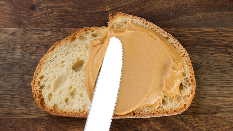 Smooth peanut butter being spread onto bread with a knife