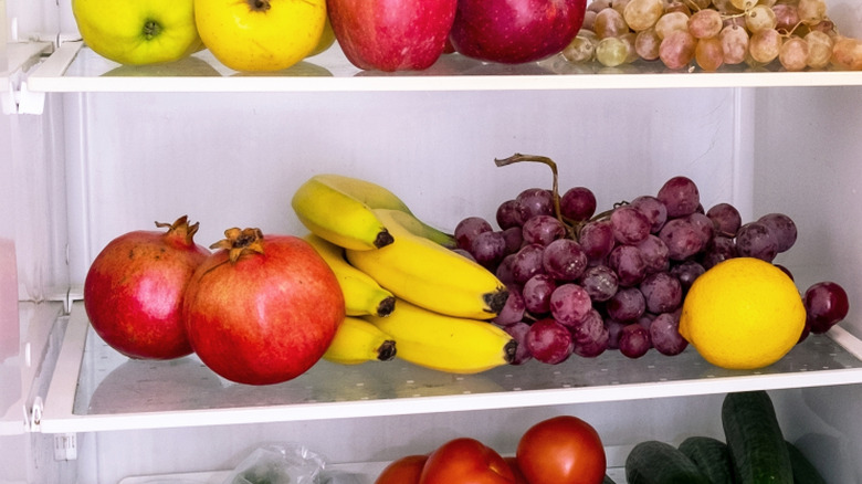 Pomegranates in fridge next to bananas, grapes, and other fruits