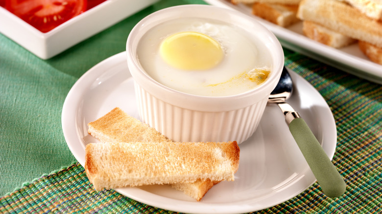 Coddled egg in bowl with toast and fresh tomatoes