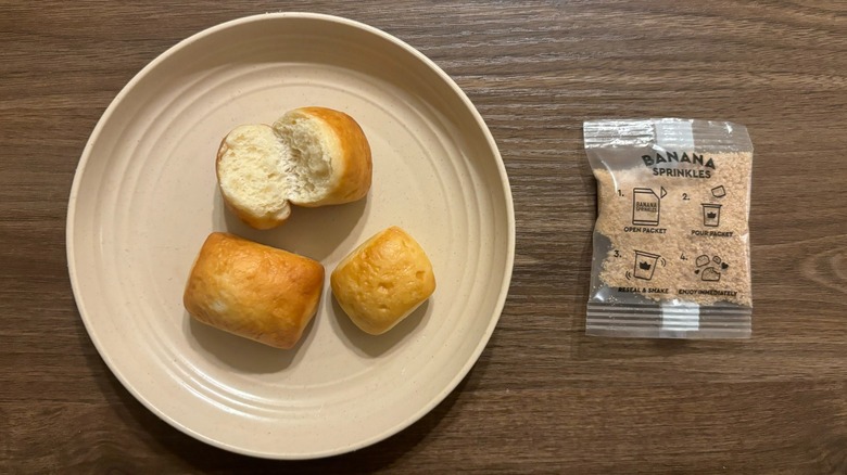 untopped King's Hawaiian x Minions Shake 'Em Banana Bites on brown plate next to packet of banana sugar