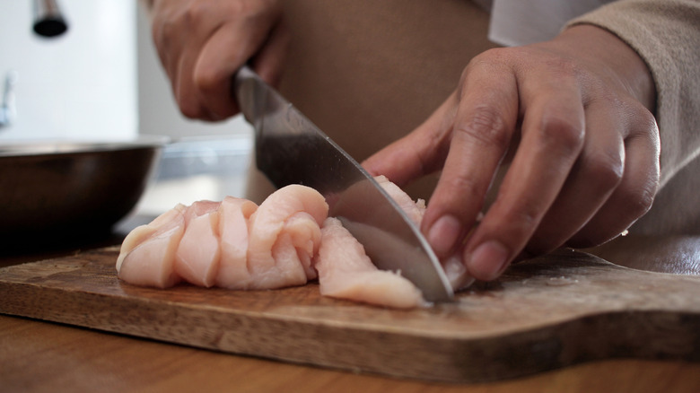 Person cutting chicken on a cutting board