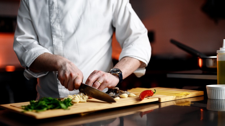Person in white shirt chopping ingredients with a kitchen knife