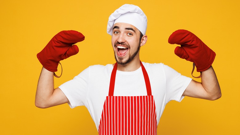 Man wearing red oven mitts and a striped apron