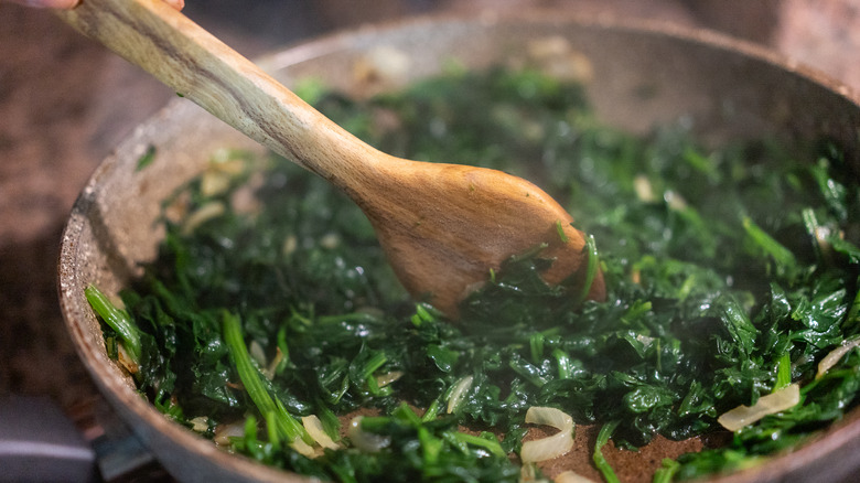 Person cooking greens with a wooden spoon