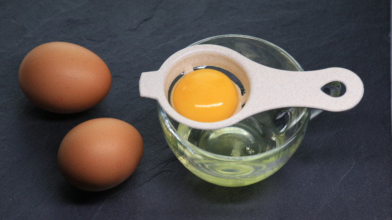 Two eggs next to an egg separator in use