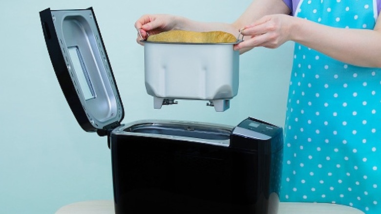 Hands removing bread in a pan from an electric bread machine
