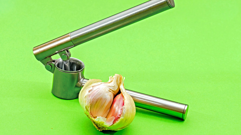 A metal garlic crusher with a bulb of garlic