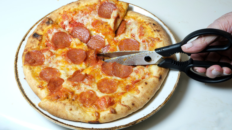 Scissors cutting a pepperoni pizza into quarters