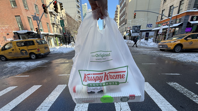a Krispy Kreme bag is held up on a crosswalk
