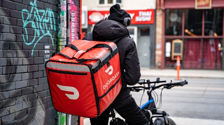 A DoorDash delivery worker on a bicycle stops and waits near street