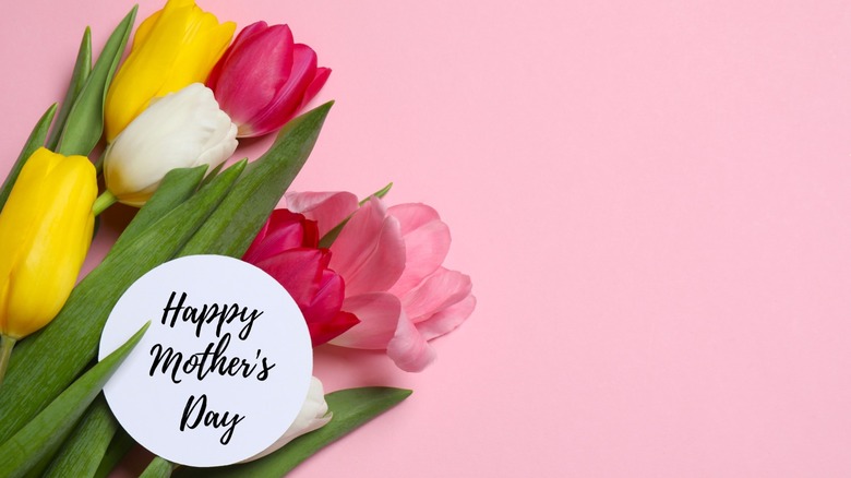 Happy Mother's day card lying over a bouquet of fresh tulips on a colored background