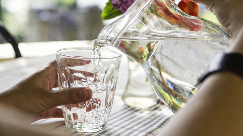 A person pours a glass of water from a jug