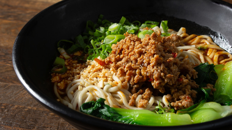 dan dan noodles with peanuts and greens in a black bowl