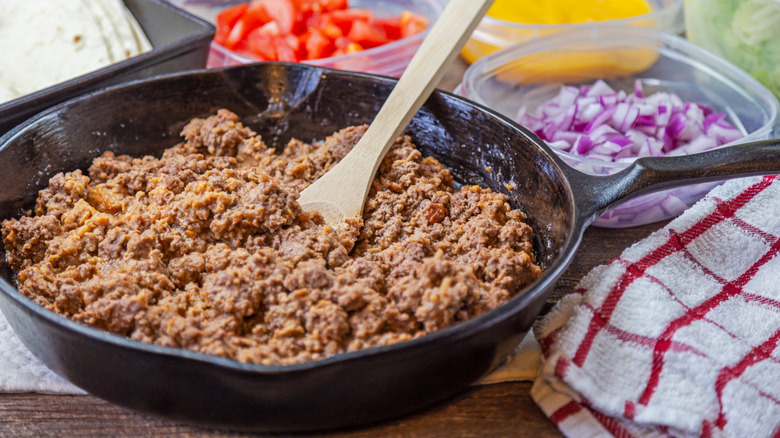 cooked ground beef in a black frying pan next to containers of chopped vegetables