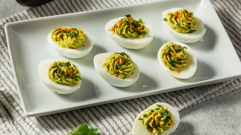 A plate of seven herbed deviled eggs, garnished with paprika and parsley