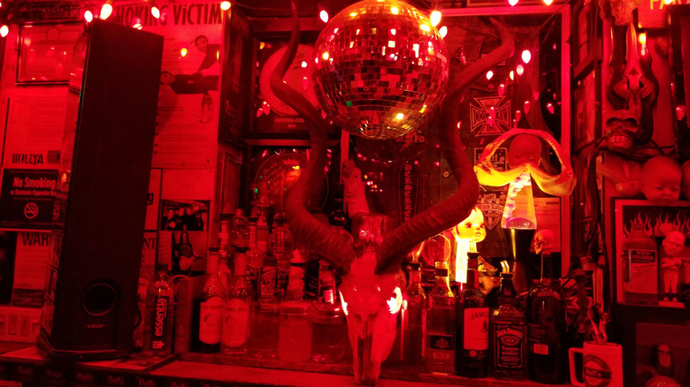 Red lighting on horned skull under a disco ball on a counter full of liquor bottles