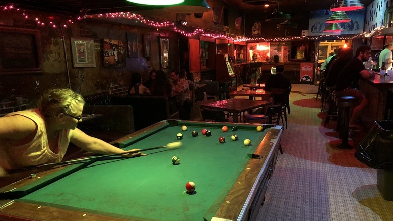 A woman shooting pool in a dive bar lit with Christmas lights