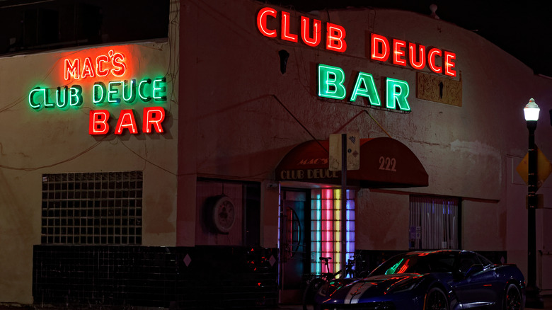 Red and green neon signs advertising Club Deuce Bar on a concrete building.