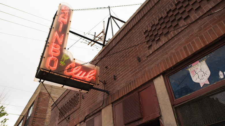 Neon sign on a brick building says Rainbo Club in red letters with a green martini glass.