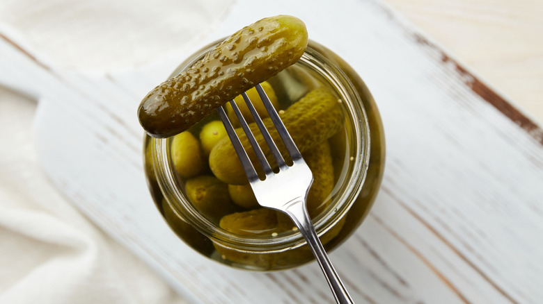 A pickle on a fork above a jar of pickles