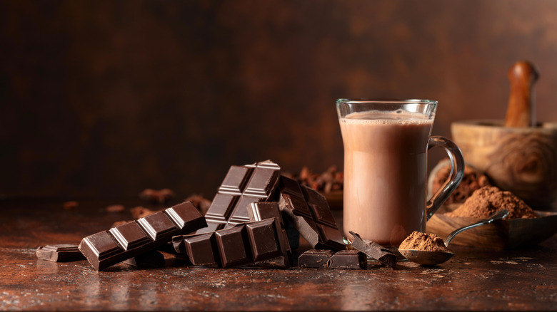 A hot chocolate sitting next to a pile of broken chocolate bars