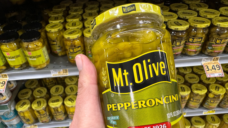 A person holds a jar of Mt. Olive pepperoncini peppers in the grocery store