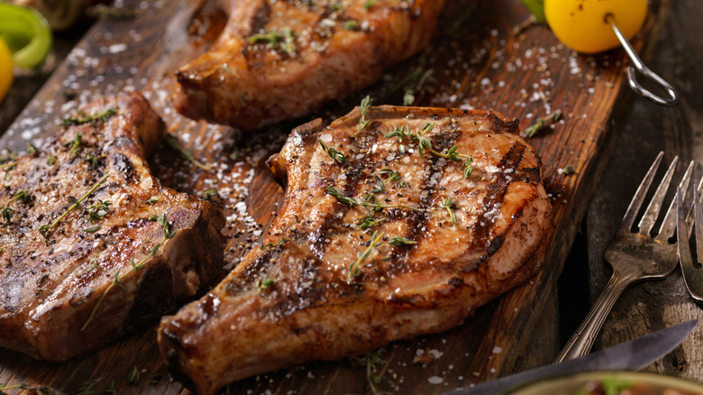 pork chops with grill marks, topped with thyme and sitting on a wooden cutting board