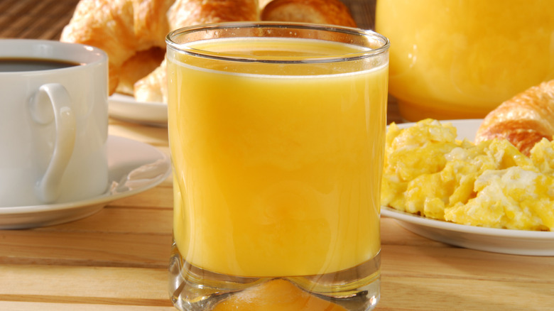 A glass of fresh orange juice with black coffee, scrambled eggs and croissants