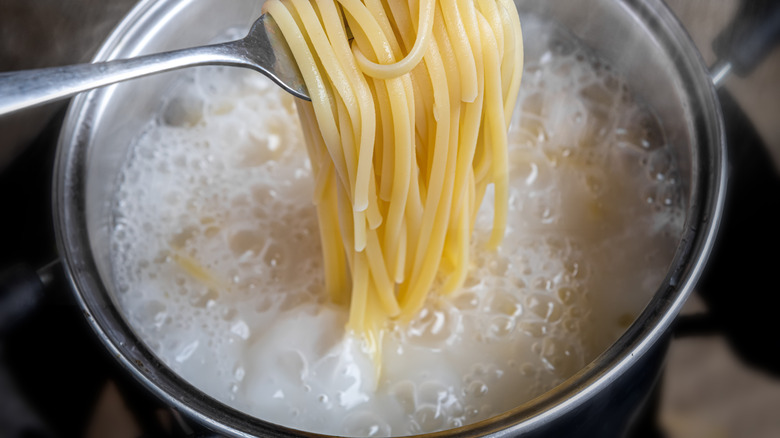 Spaghetti noodles cooking in starchy boiling water in a pot with indoor low lighting.