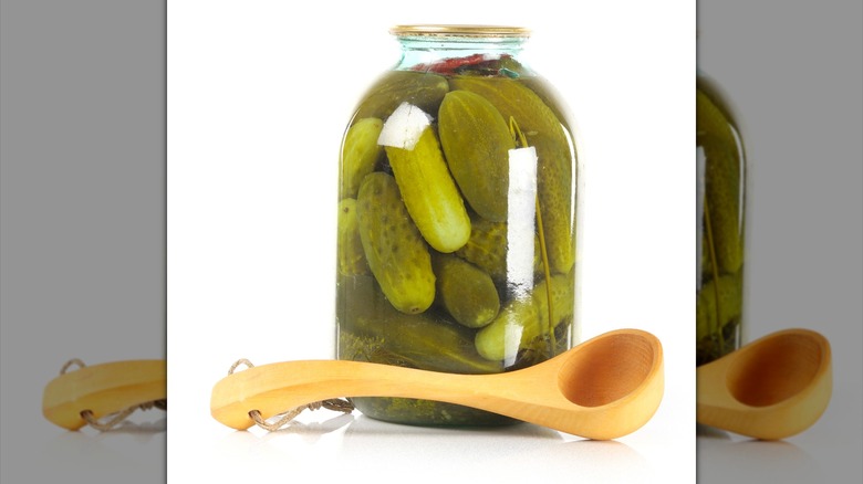 Pickled cucumbers in a glass jar with a big wood spoon. isolated on white.