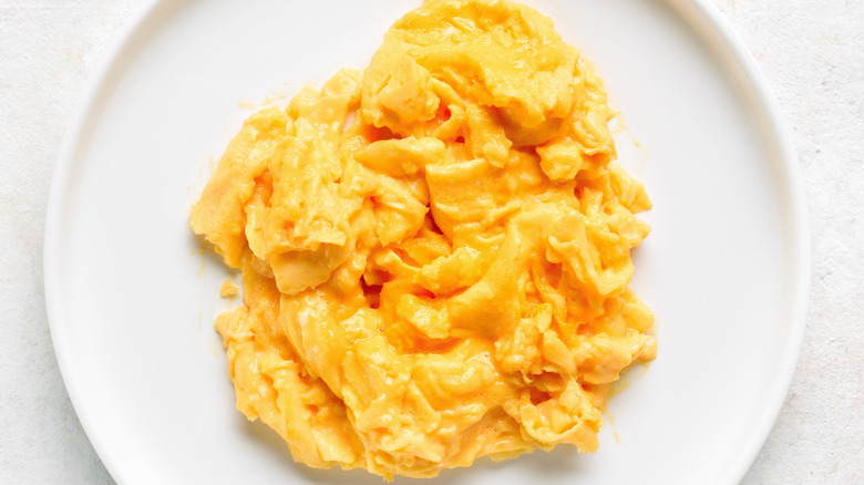 Close up view of scrambled eggs on white plate on light background.