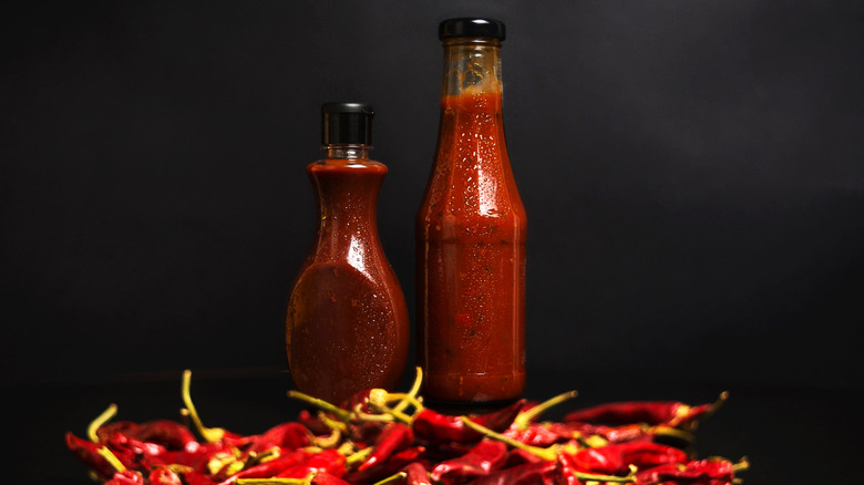 Bunch of dried chilly peppers in front of two sweating bottles of red spicy sauce