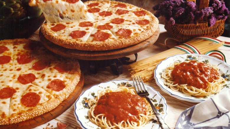 Two pizzas and plates of spaghetti with marinara