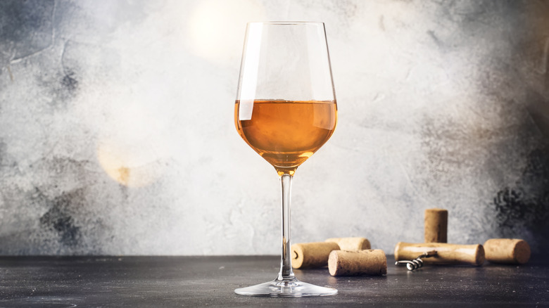 A glass of orange wine with a corkscrew and several corks