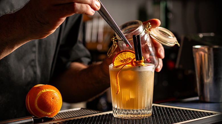 Hands preparing a short orange cocktail