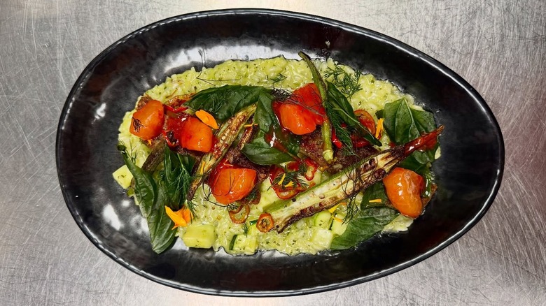 A professionaly plated meal on a black plate sitting on a prep table
