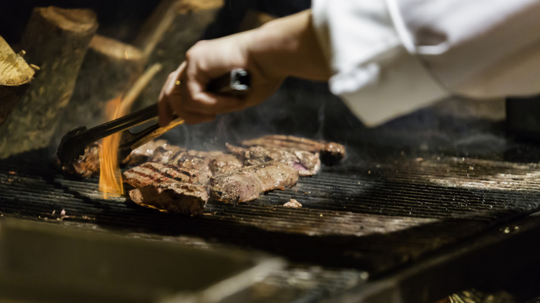 A chef cooking steak on a grill