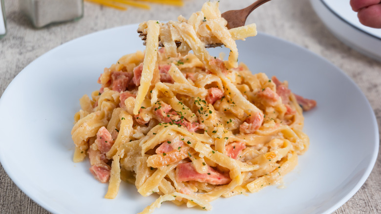 Creamy fettuccine pasta dish with ham on a white plate