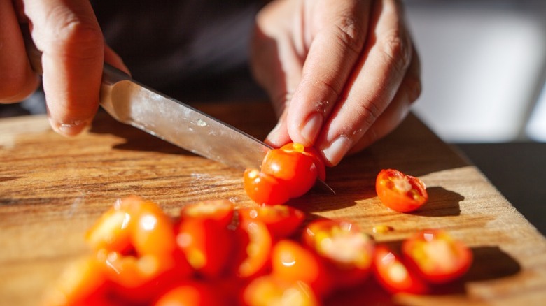 A cook cutting tomatoes on a wooden cutting board.