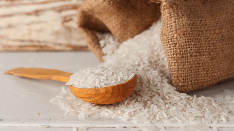 Burlap sack and wooden scoop with grains of white rice spilling out