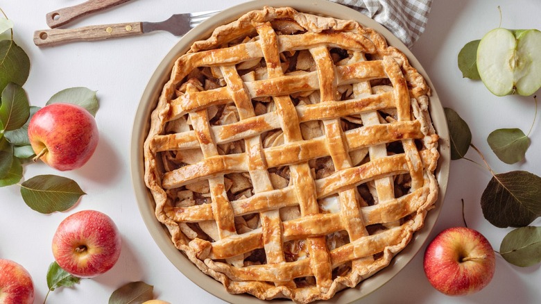 A lattice-topped apple pie surrounded by fresh apples