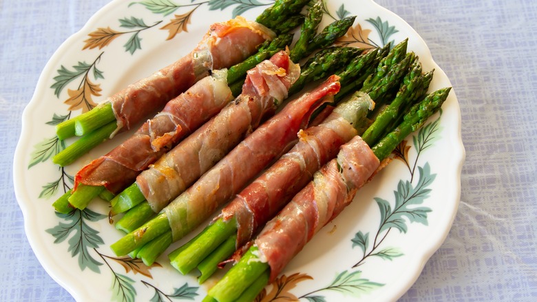 A closeup of prosciutto-wrapped asparagus spears on a plate