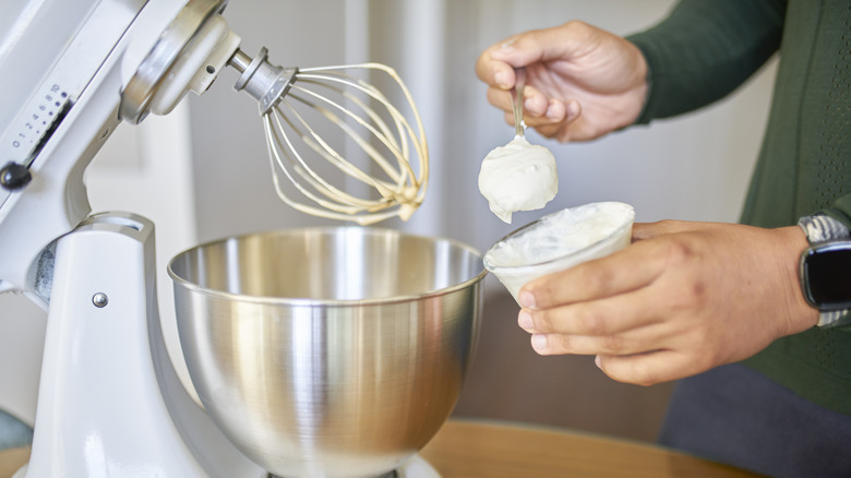 A baker adding a spoonful of yogurt to cake mix in a mixer.