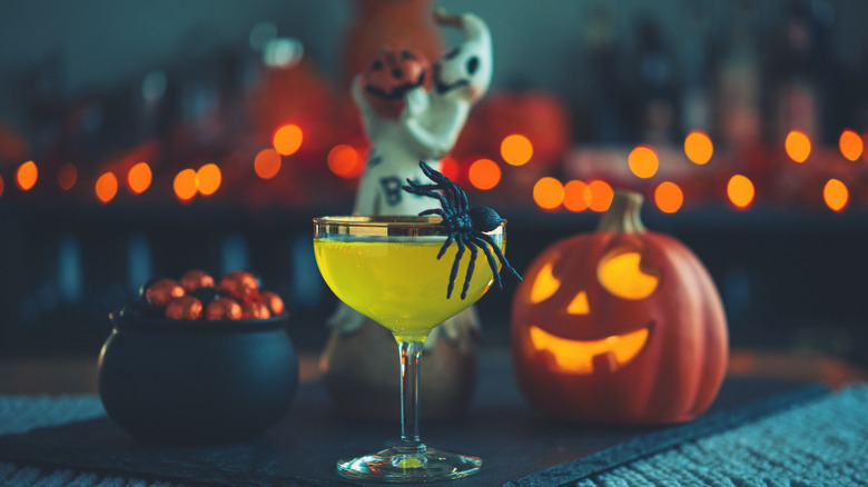 Halloween cocktail with jack o' lantern, bowl of candy, ghost decor, and fake spider
