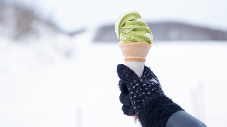 Gloved hand holding ice cream cone while outdoors in snow