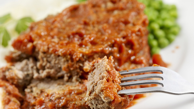 Fork stabbed into a piece of meatloaf with tomato sauce