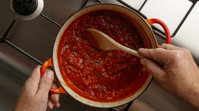 Person stirring tomato pasta sauce in a pot on the stove