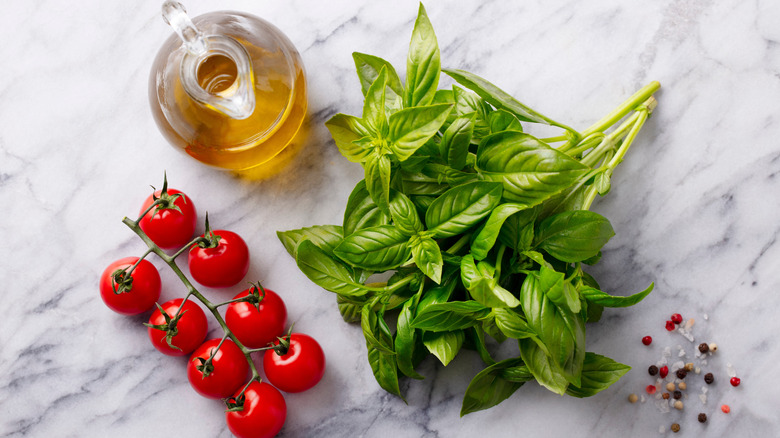Top view of bottle of olive oil, cherry tomatoes, and bunch of fresh basil