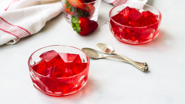 Two small bowls of Jell-O with spoons and a cup of strawberries on a table.