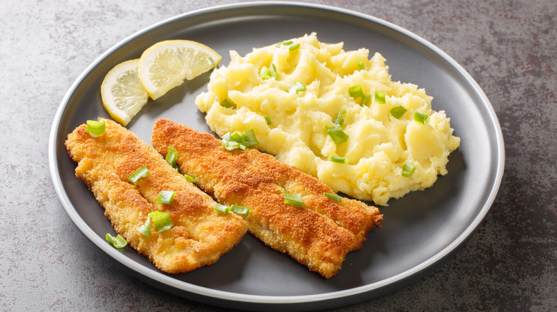 Breaded fish fillets alongside mashed potatoes and lemon slices